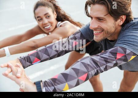 Image of a happy cheery young strong sports couple man and woman make stretching exercises outdoors. Stock Photo
