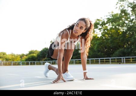 Photo of african american nice woman in sportswear doing exercise while working out at playground outdoors Stock Photo
