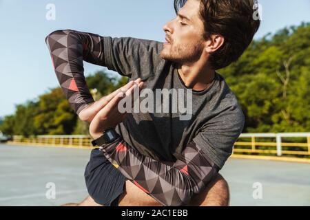 Photo of handsome concentrated man in sportswear doing exercise while working out at playground outdoors Stock Photo