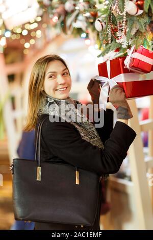 Picture of happy woman with glass in hands near boxes with gifts ,decorated spruce branches on street in evening Stock Photo