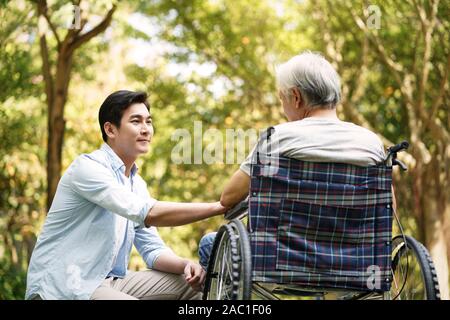 asian son talking to and comforting wheelchair bound father Stock Photo