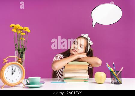 Image of young relaxed girl sitting at desk and sleeping on stack of books with thought bubble above her head isolated over violet background Stock Photo