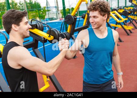 Two happy fitness men working out outdoors at the playground, greeting each other Stock Photo
