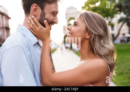 Image of amazing positive cute young loving couple walking by street outdoors looking at each other. Stock Photo