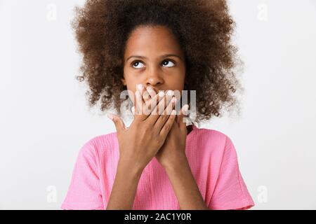 Shocked little african girl wearing pink blouse standing isolated over white background, looking away, covering mouth Stock Photo