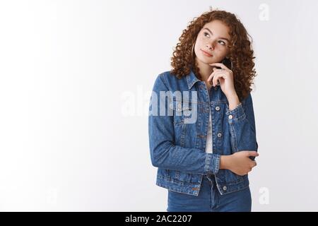 Dreamy thoughtful cute ginger girl curly-haired wearing denim lean head look upper left corner thinking making choice mind decide what food order Stock Photo