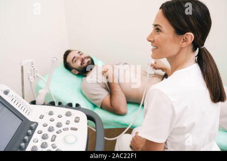 Image of happy man getting abdominal ultrasound scan by female doctor in medical uniform at hospital Stock Photo