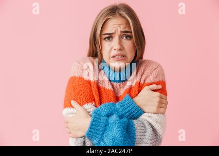 Portrait of a beautiful young lovely frozen girl wearing sweater standing isolated over pink background, shivering Stock Photo