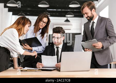 Photo of multinational focused colleagues discussing project and smiling while working in open-plan office Stock Photo