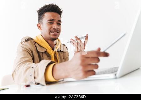 Image of confused african american guy using cellphone and tablet computer while working with laptop in white office Stock Photo
