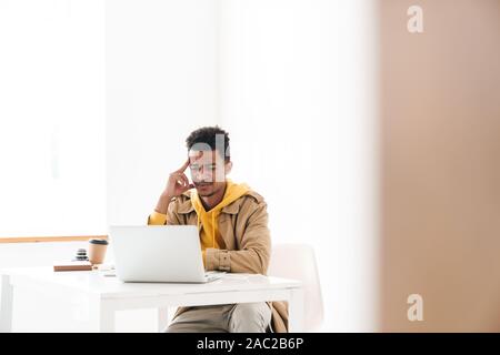 Image of perplexed african american man using laptop computer while working in white office Stock Photo