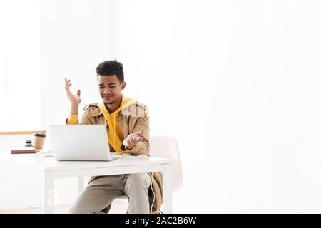 Image of displeased african american man using laptop computer while working in white office Stock Photo
