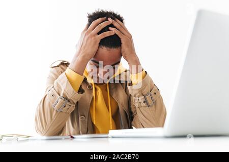 Image of frustrated african american man grabbing his head while working on laptop computer in white office Stock Photo