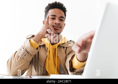 Image of perplexed african american man thinking while working on laptop computer in white office Stock Photo