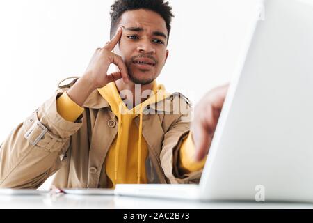 Image of concentrated african american man thinking while working on laptop computer in white office Stock Photo