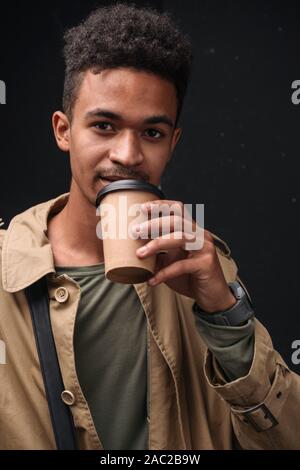 Image of masculine african american guy in coat drinking coffee takeaway isolated over black background Stock Photo
