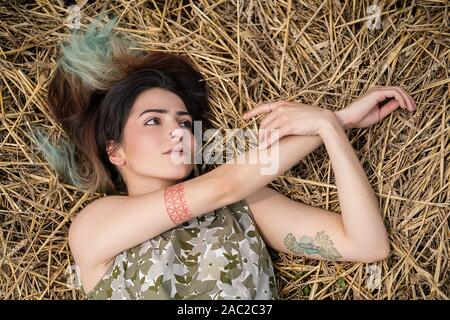 Girl lying in a wheat field and posing on hay dry grass, summer season. Relaxing in nature. Young woman posing in field. Mindset reset Stock Photo