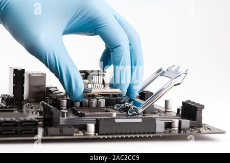 Computer technician wearing blue gloves installing CPU into motherboard. Stock Photo