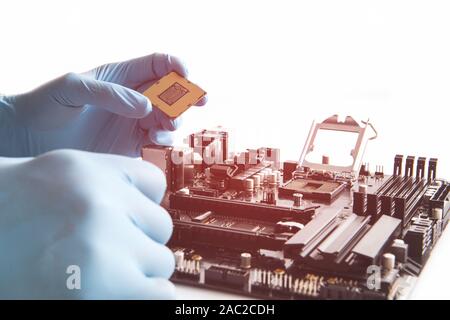 Computer technician wearing blue gloves installing CPU into motherboard. Stock Photo