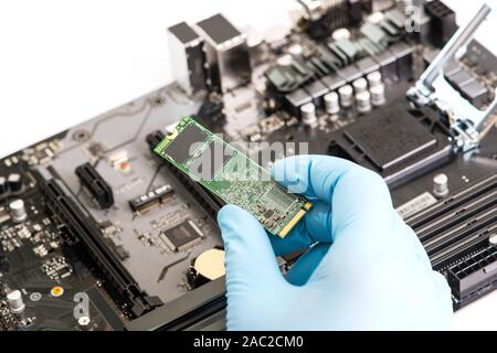 Close-up of Installing ssd hard drive disk into motherboard. Hand in blue glove holds ssd hard drive disk. Stock Photo