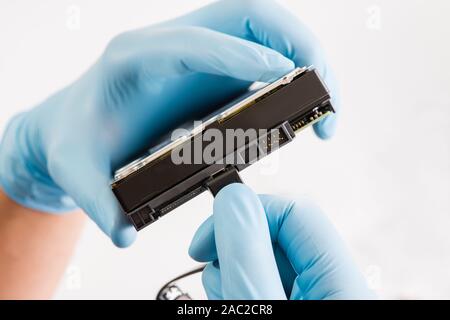 Repairman hand in blue runnber glove holds computer hard drive disk with green chip. white background. Stock Photo