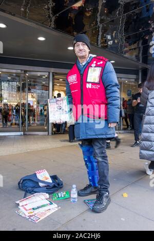 Male Big Issue seller outside John Lewis Department Store on London's Oxford Street, London, England, UK Stock Photo