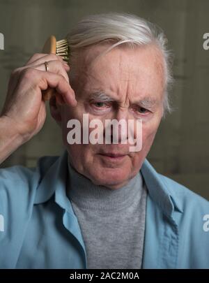 Elderly man combing himself hair. Stock Photo