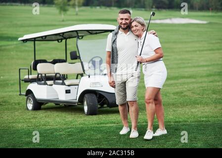 Couple of two golfers staying on the green lawn with cart behind of them Stock Photo