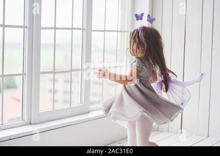 Motion photo. Nice little girl in the fairy tale wear going to the windows to look what's outside Stock Photo