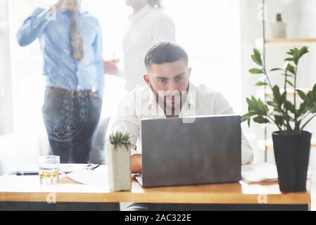 Bearded man working with laptop in office room with two employees at background Stock Photo