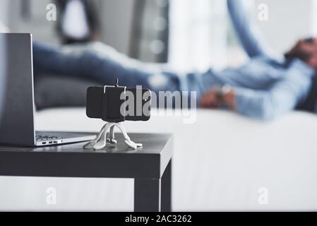 Close up photo of smartphone standing on the tripod with lying man at background Stock Photo