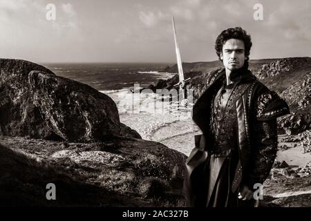 Black and white portrait of handsome knight holding sword and pointing to coastline in the background Stock Photo