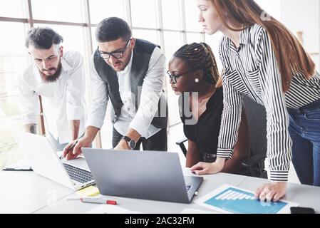 Man in the glasses explains the essence of the task. Four multiracial employee have work in the office using the laptop on table Stock Photo