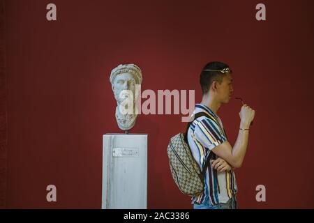 Athens, Greece - August 17, 2019: Tourist wear crown admire male head statue of marble in red wall Hadrien's library Stock Photo