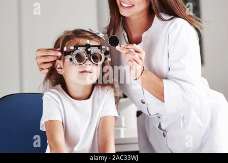 When job gives you a smile. Doctor checking little girl sight and tuning the phoropter Stock Photo