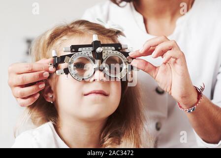 Difficult to see that word. Doctor checking little girl sight and tuning the phoropter Stock Photo