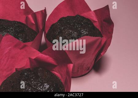 Three brown baked chocolate muffins rolled in pink paper and placed on matte dark pink background with copy space Stock Photo