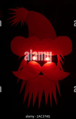 Scary looking Santa Claus head made from paper and eyes illuminated by red light on black background with copy space Stock Photo