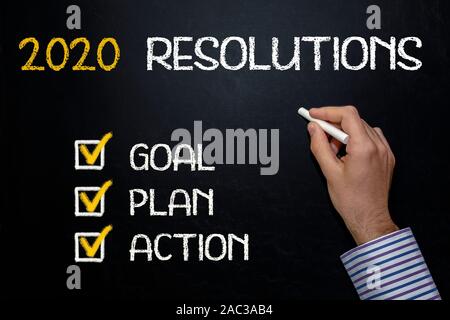 Human Hand Writing New Year 2020 Resolutions on Chalkboard Stock Photo