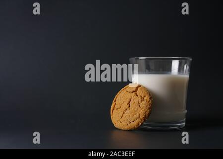 A ginger molasses cookie leans up against a glass of cold milk on a black background with copy space on the left Stock Photo