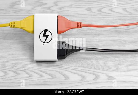 A yellow cable, an orange and a black one connected to a multiple socket over a white wood background, with the energy symbol on the socket Stock Photo