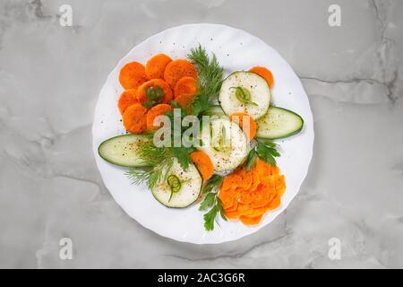 Festive slicing of fresh vegetables with parsley and dill on a white plate on a gray marble background. Stock Photo
