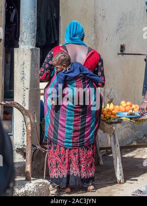 Dakar, Senegal - February 3, 2019: Senegalese woman in colorful clothes with child on her  back. Africa. Stock Photo