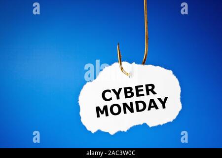 Text Cyber Monday printed on a piece of paper hanging on a fishing hook over blue background. Beware of the Cyber Monday sale trap concept. Stock Photo