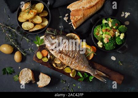 Oven fresh gilthead baked with herbs and lemon, served with potatoes and buttered broccoli with almond flakes Stock Photo