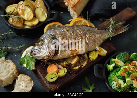 Oven fresh gilthead baked with herbs and lemon, served with potatoes and buttered broccoli with almond flakes Stock Photo
