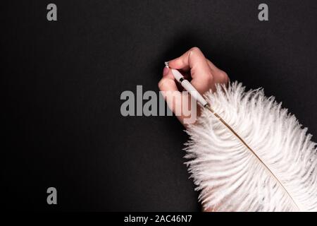 Female hand holding feather pen over black background Stock Photo