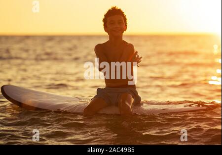 silhouette of a boy on a surfboard in a calm sea enjoys the sunset Stock Photo