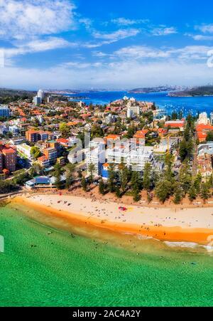 Manly beach in vertical aerial view over waterfront of sandy strip to distant Sydney Harbour and city CBD high-rise towers on horizon. Stock Photo