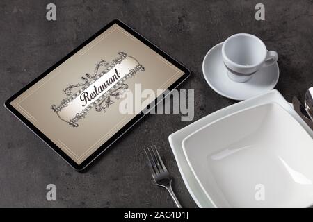 Tablet with stylish restaurant logo and laid table Stock Photo